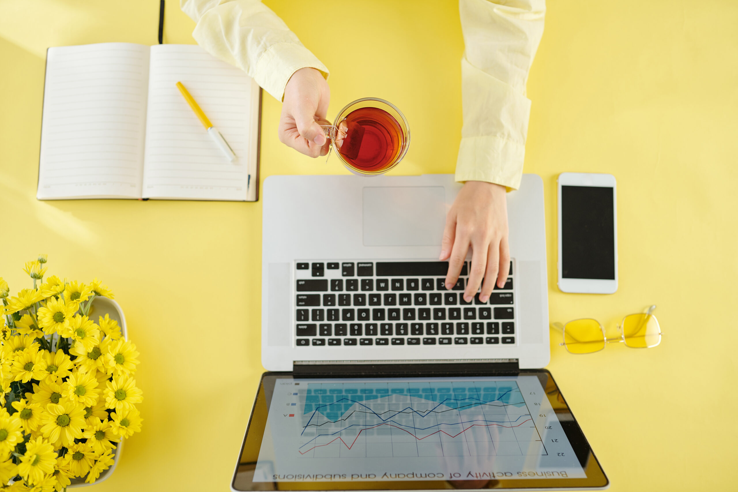 Hands of businesswoman drinking cup of hot black tea and working on laptop at home