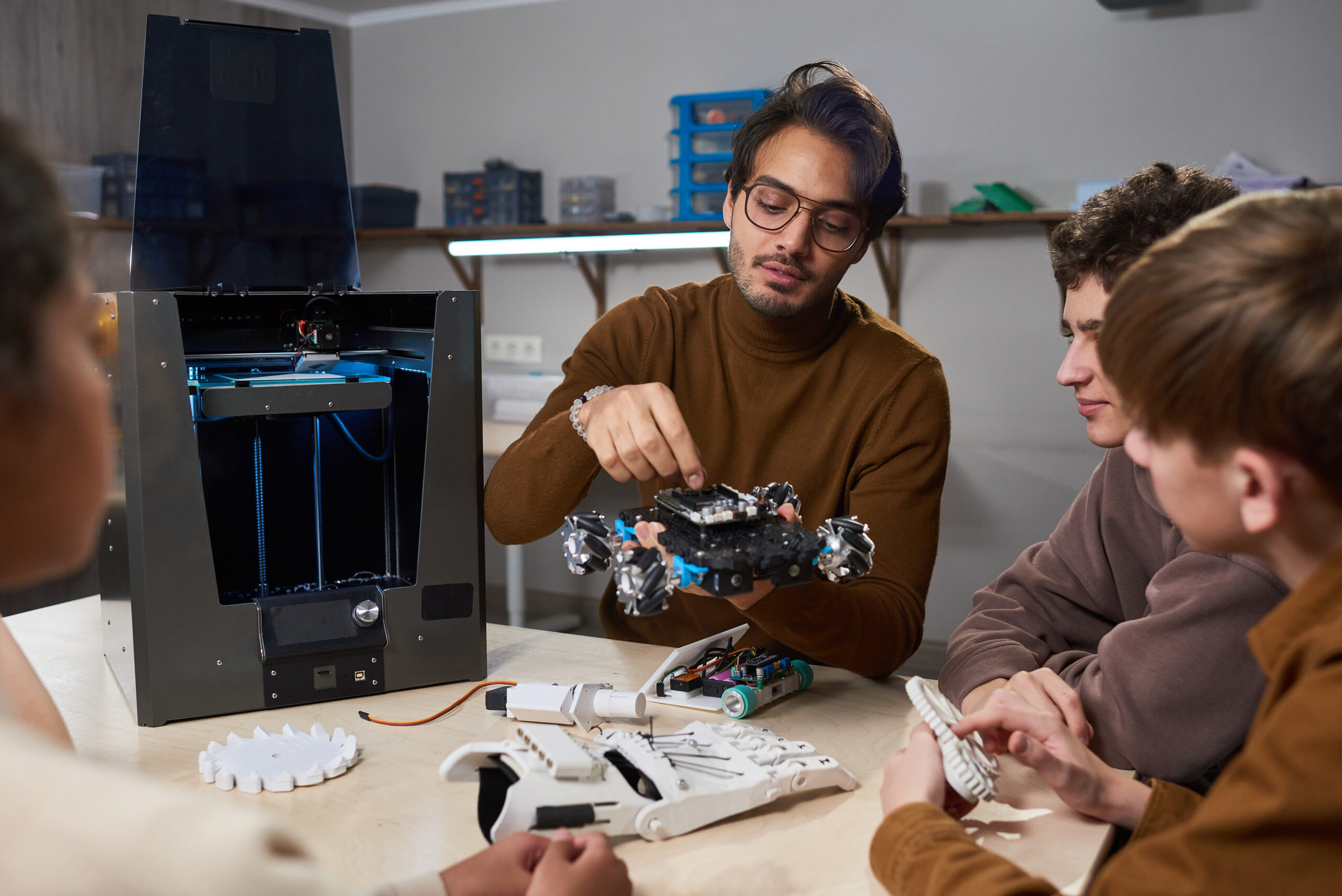 Young teacher showing his students how to build robotic machine while they sitting at the table during lesson at science school